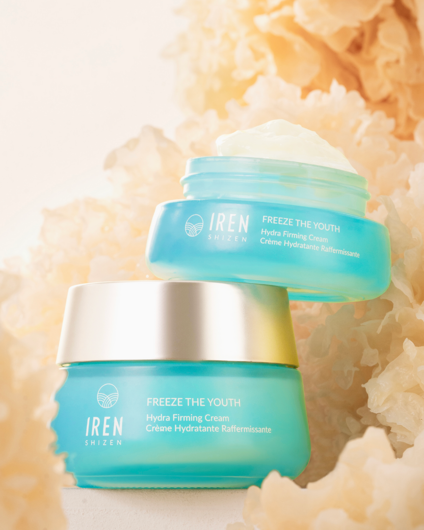 Image of two blue jars of FREEZE THE YOUTH Hydra Firming Cream by IREN Shizen with the age-defying formula, placed among light brown decorative fibers. The cream, enriched with snow mushroom extract, is visible in the top jar, which is open, while the bottom jar is closed. #all-groups