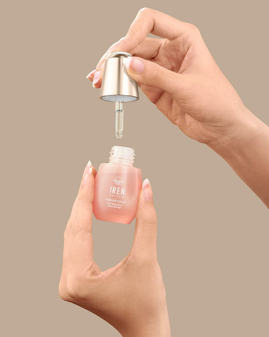 A hand is holding a bottle of custom ONSEN skincare FOREVER YOUNG Anti-Aging Serum by IREN Shizen on a beige background.
