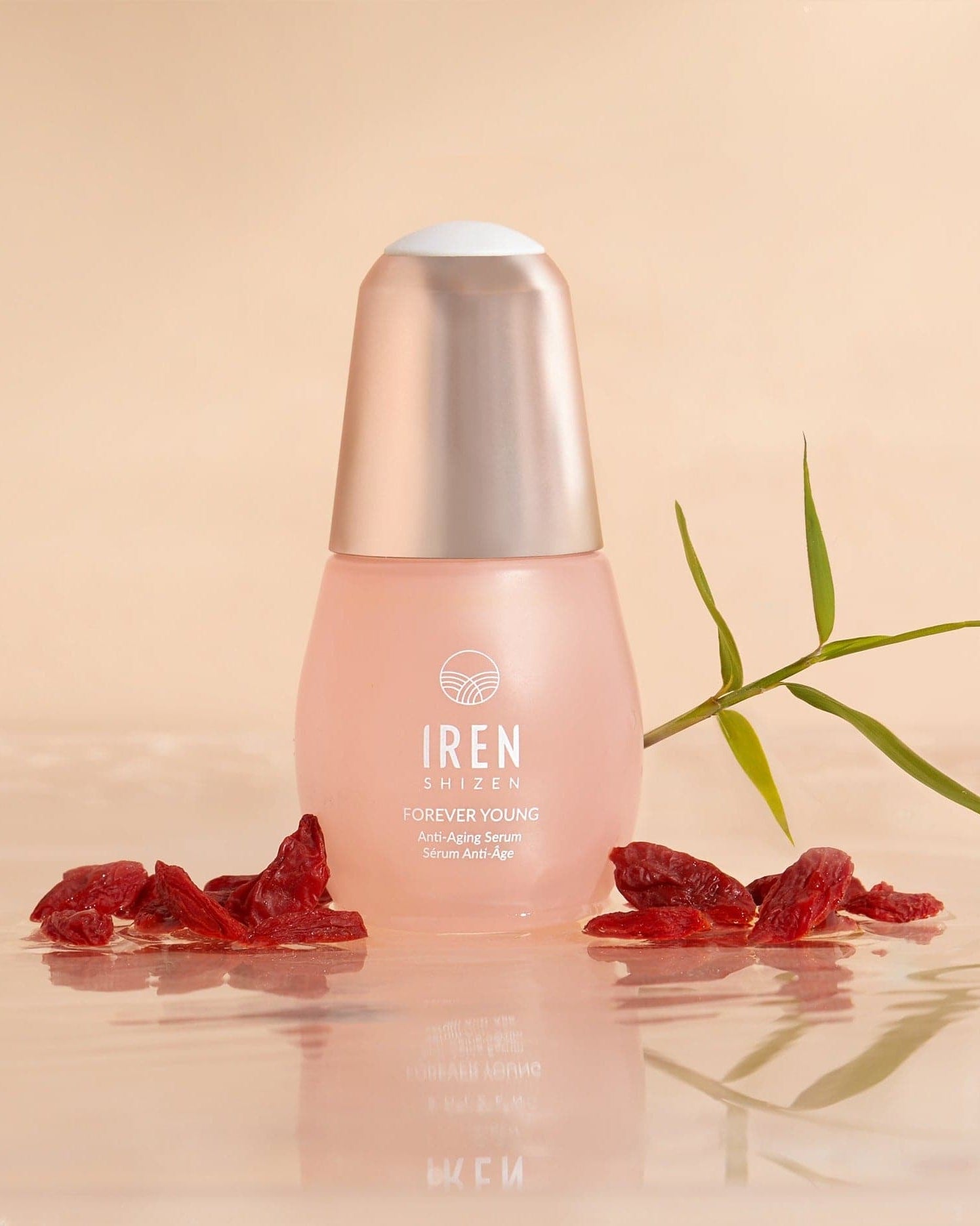 Close-up of the IREN Shizen APAC TIMELESS ELIXIR Anti-Aging Eye Skincare Kit bottle surrounded by dried red berries and a green leaf on a reflective surface with a beige background, showcasing the allure of anti-aging skincare.