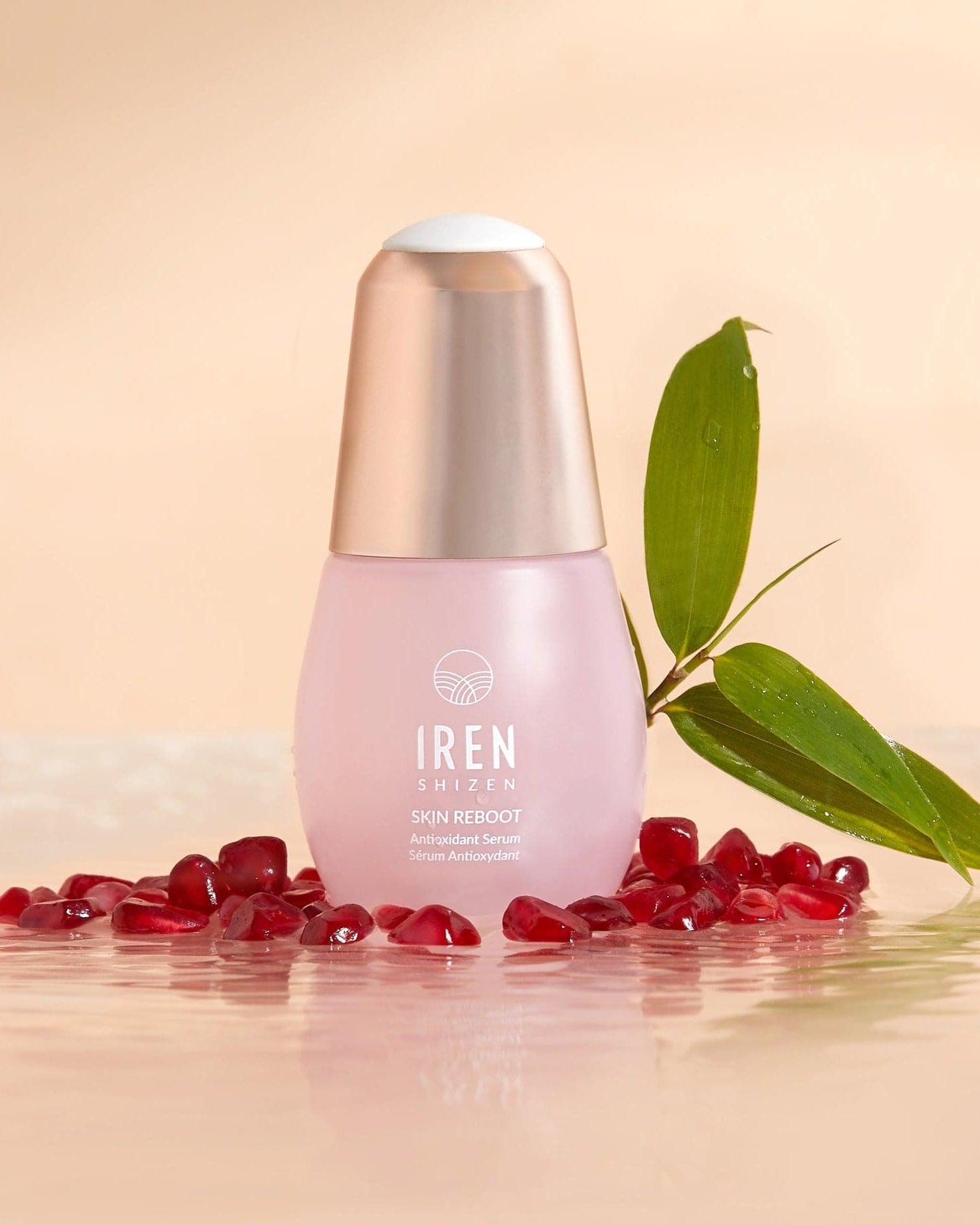 A pink bottle labeled "IREN Shizen APAC TIMELESS ELIXIR Anti-Aging Eye Skincare Kit" sits elegantly on a glossy surface, surrounded by pomegranate seeds and a green leaf, epitomizing the essence of premium anti-aging serums.