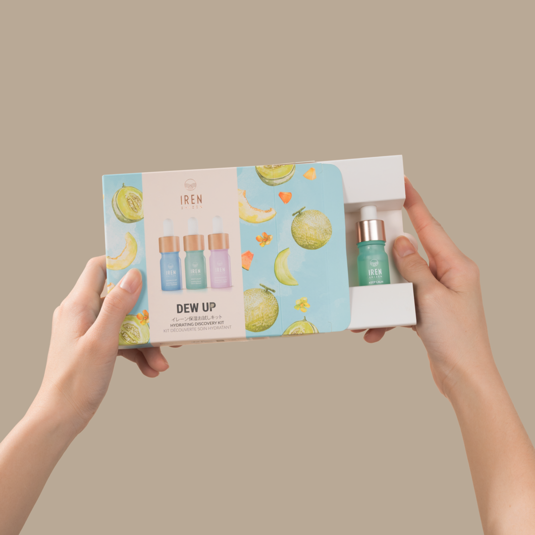 A hand holding a box with a bottle of juice and serum, providing hydration and protection with the DEW UP Hydrating Discovery Kit from IREN Shizen.